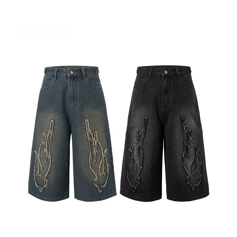 Men's black cropped denim shorts with a red and yellow flame embroidery patch on the leg.