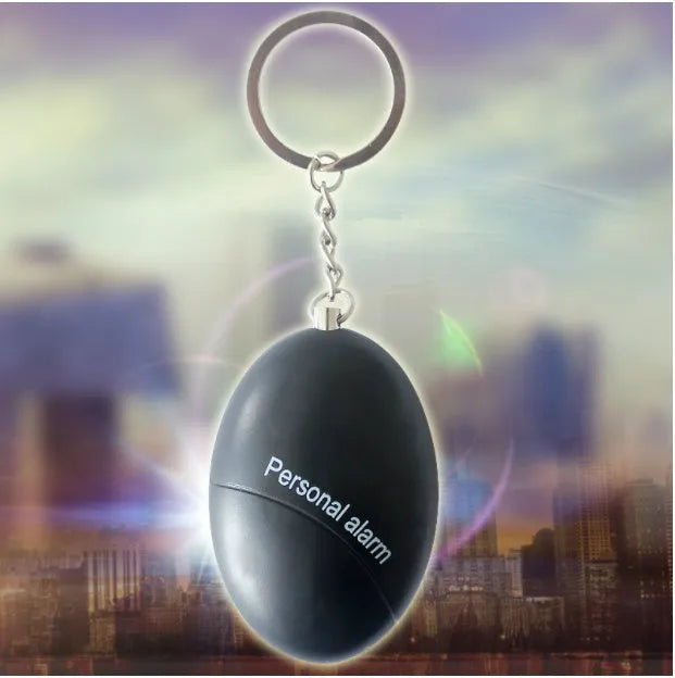 Compact black personal alarm keychain with pull-ring for loud siren activation, shown next to a ruler showing 6cm length.