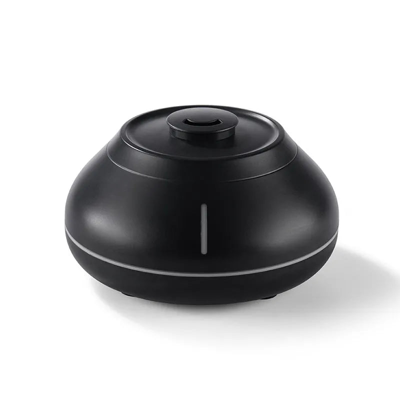 White rounded desktop aroma diffuser with colourful flame-like light and mist plume on a wooden table.