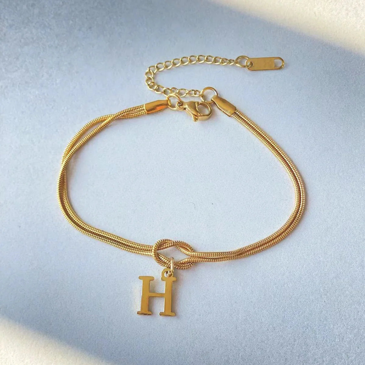 Elegant letter charm bracelets for women in gold and silver tones, featuring a delicate snake chain design and personalised letter charms.