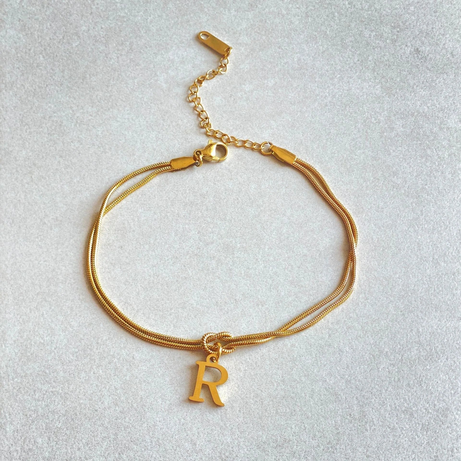 Elegant letter charm bracelets for women in gold and silver tones, featuring a delicate snake chain design and personalised letter charms.