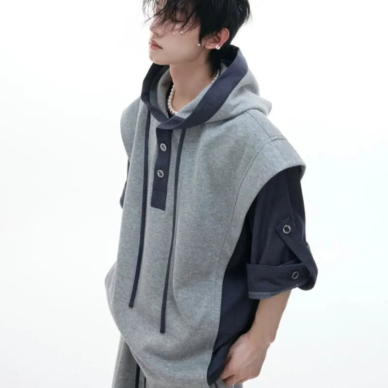 Man wearing a grey hooded short-sleeve tracksuit jacket with black trousers, showing three-dimensional stitching detail.