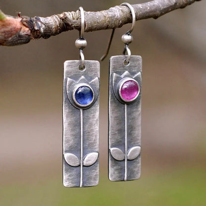 A pair of antique-finish geometric earrings with a red sapphire stone in an elliptical silver-tone setting.