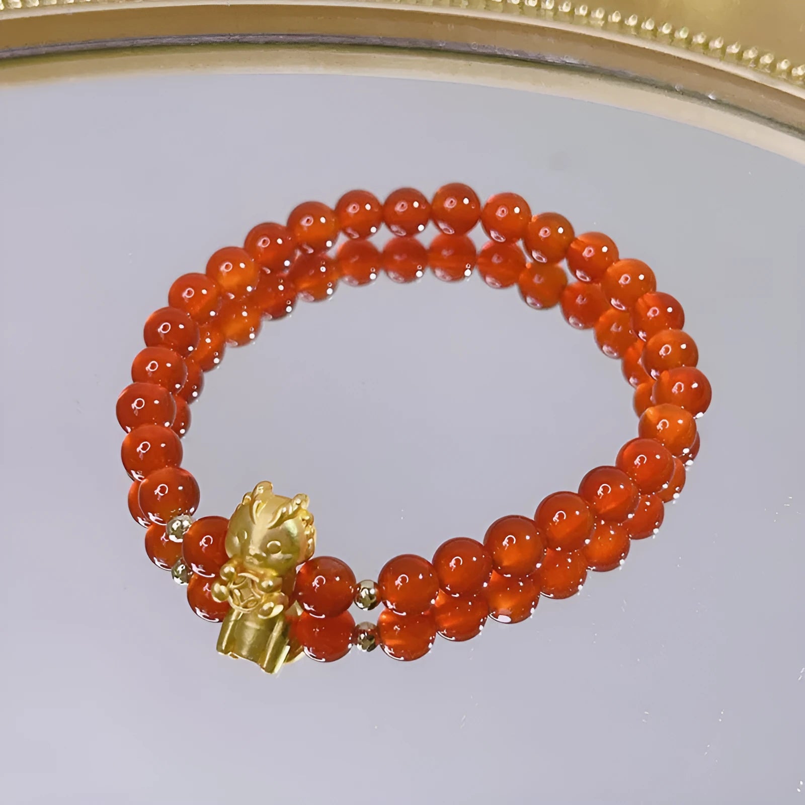 Close-up of a red agate bracelet with a dragon charm and Lucky Bag symbol on a wrist.
