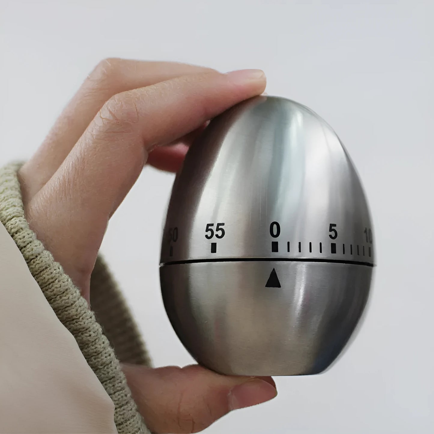 Stainless steel egg-shaped mechanical kitchen timer on a countertop.