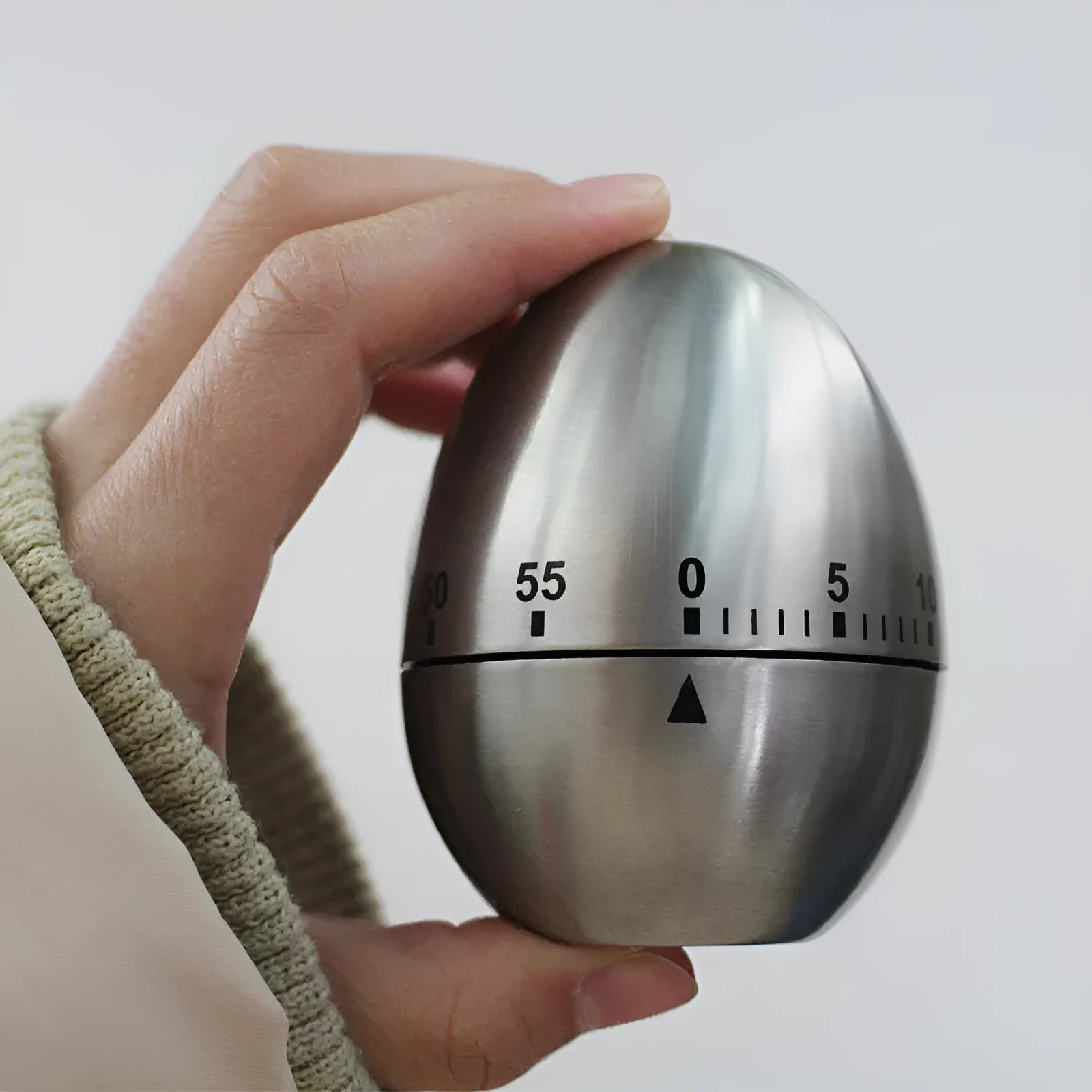 Stainless steel egg-shaped mechanical kitchen timer on a countertop.