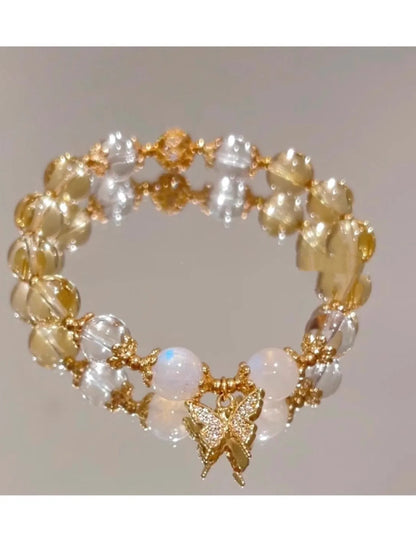 Close-up of a citrine-coloured crystal bracelet with diamond-shaped beads and a butterfly charm.