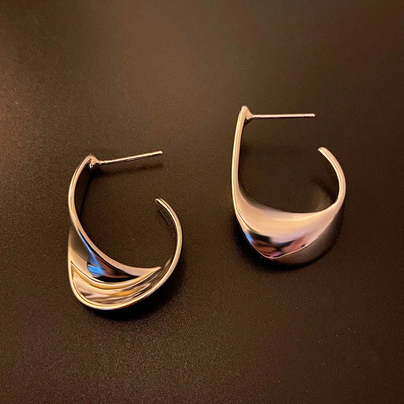 A pair of gold twisted geometric metal earrings with a round detail on a white background.