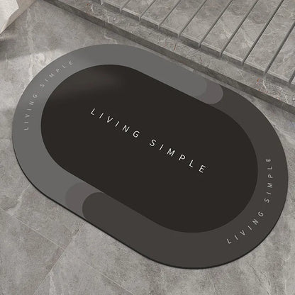 Oval grey bath mat with non-slip rubber bottom on a tiled floor, showing absorbent fabric surface