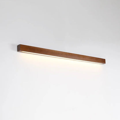 Slim walnut-coloured wooden strip wall lamp with acrylic light diffuser mounted on a plain wall.
