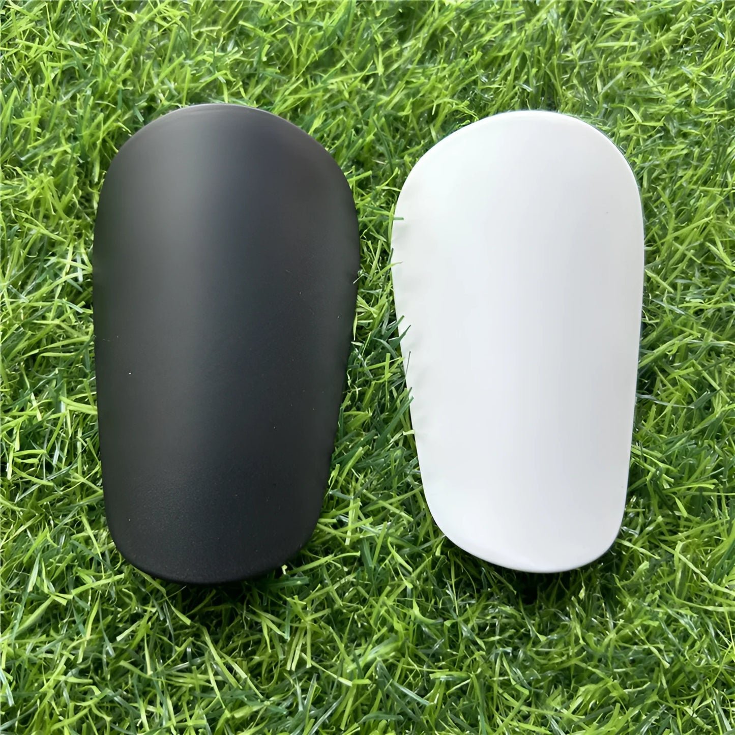 Extra small 8x5cm black and white plastic football shin guards for junior players.