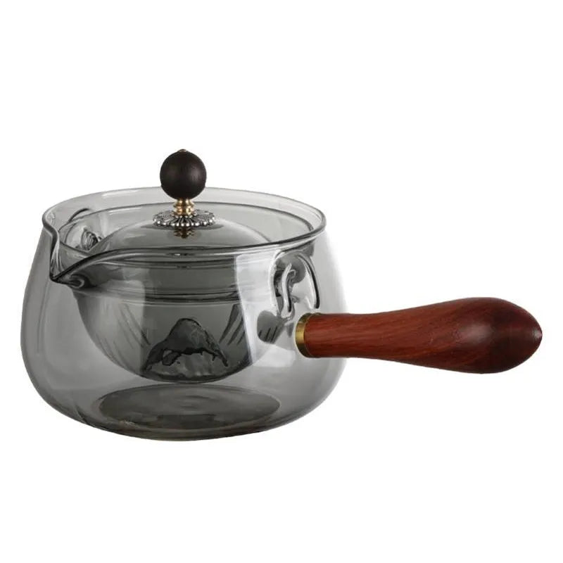 Transparent borosilicate glass rotary teapot with wooden handle and built-in infuser on a wooden surface