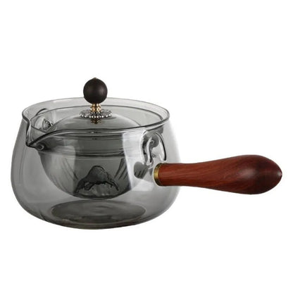 Transparent borosilicate glass rotary teapot with wooden handle and built-in infuser on a wooden surface