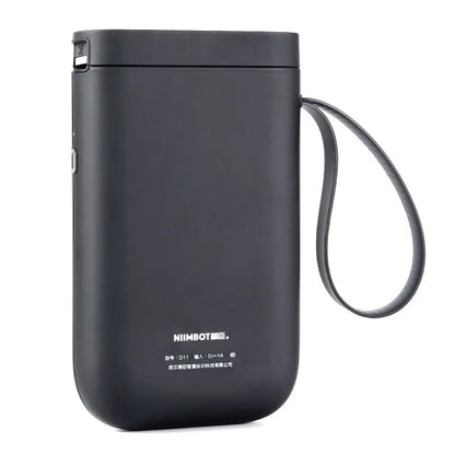 D11 black Bluetooth thermal label printer on a desk next to a smartphone showing the label design app