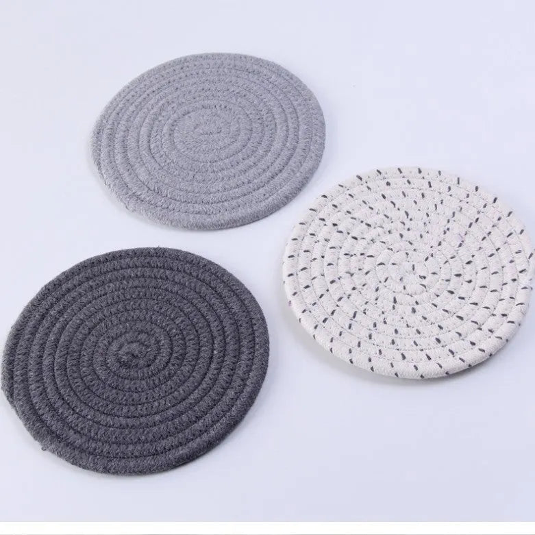 Three round grey cotton cord coaster placemats on a wooden table, each 18cm in diameter.
