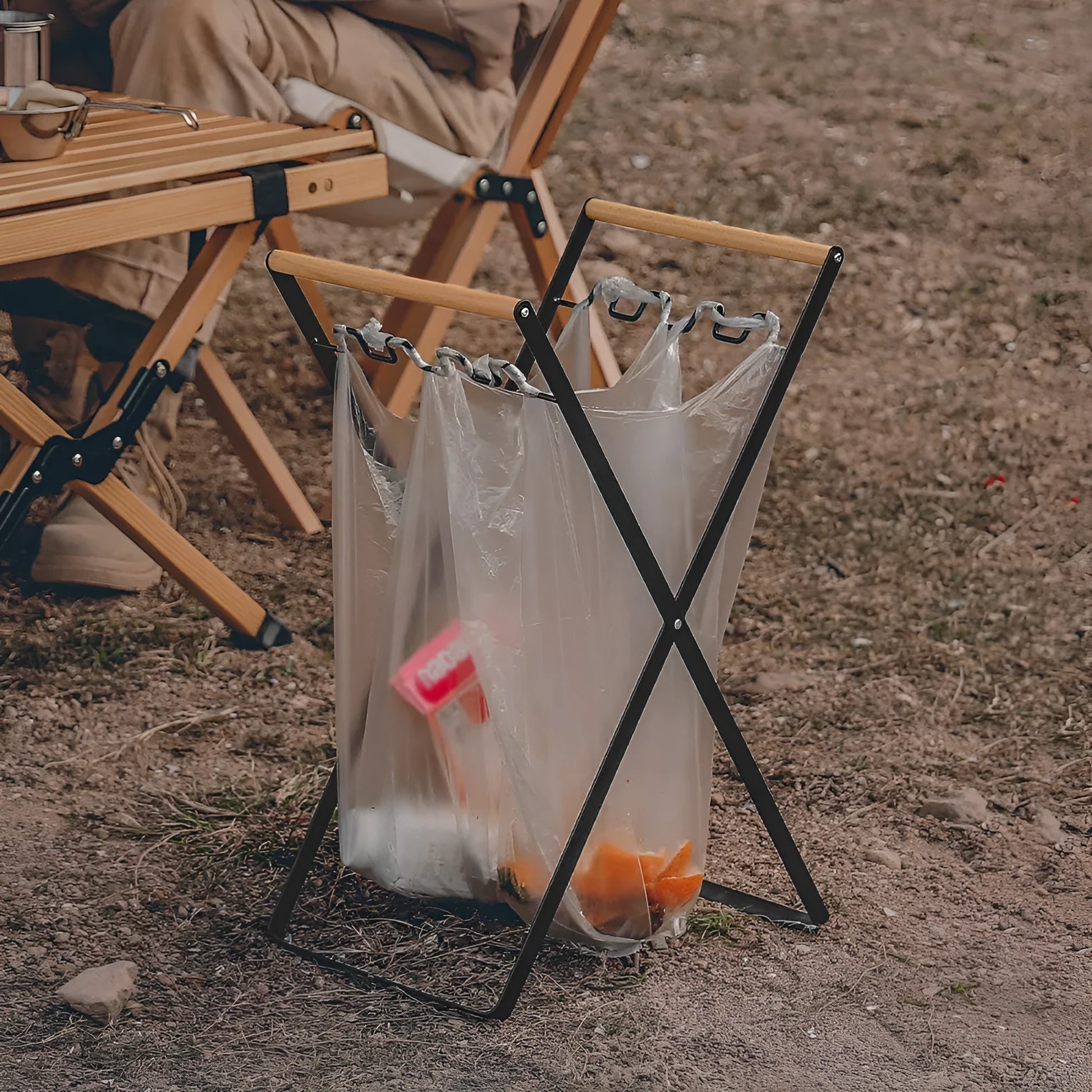Black outdoor folding trash rack with wooden handle, holding a waste bag.