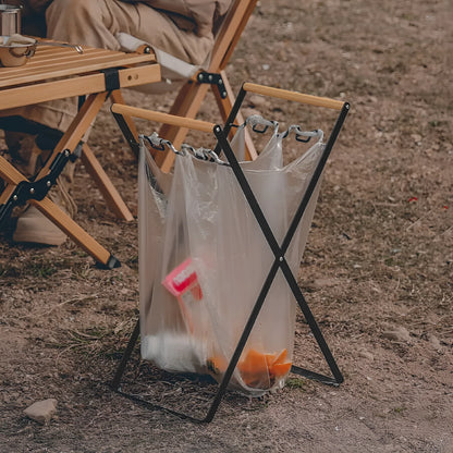 Black outdoor folding trash rack with wooden handle, holding a waste bag.