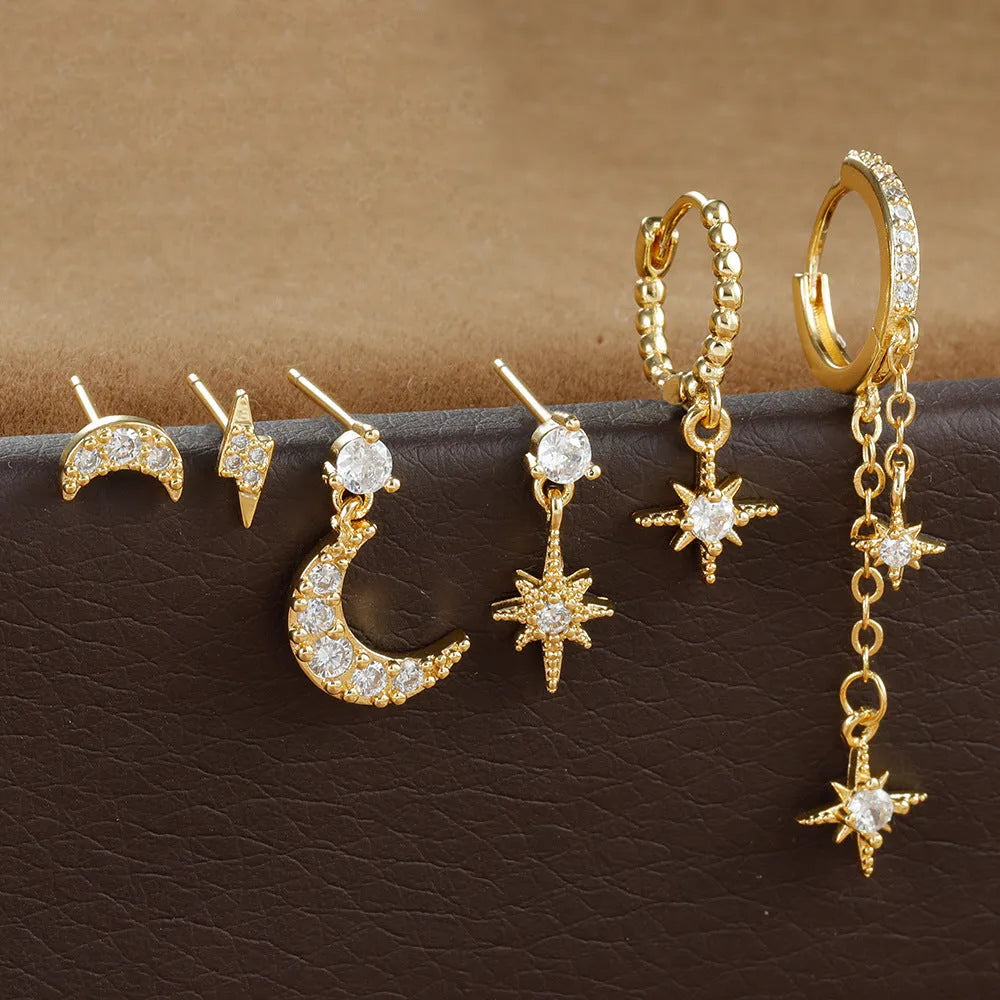 Set of six gold-coloured XINGX chain tassel stud earrings with zircon details on a flat surface.