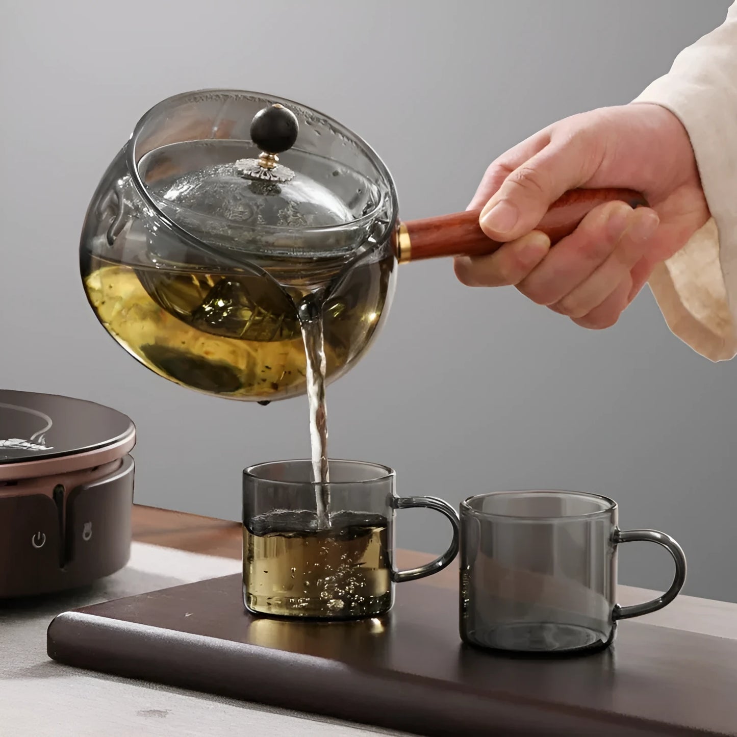 Transparent borosilicate glass rotary teapot with wooden handle and built-in infuser on a wooden surface