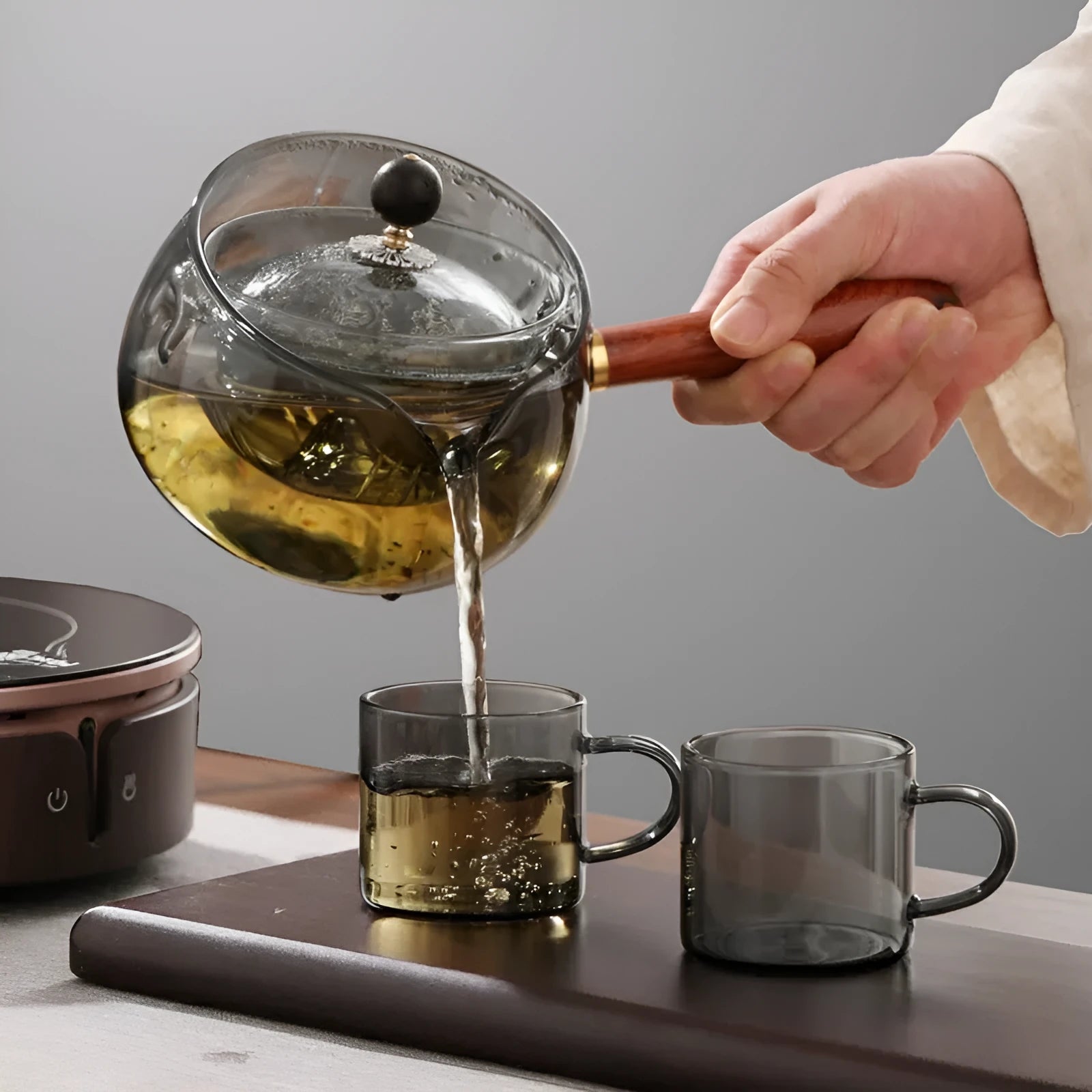 Transparent borosilicate glass rotary teapot with wooden handle and built-in infuser on a wooden surface