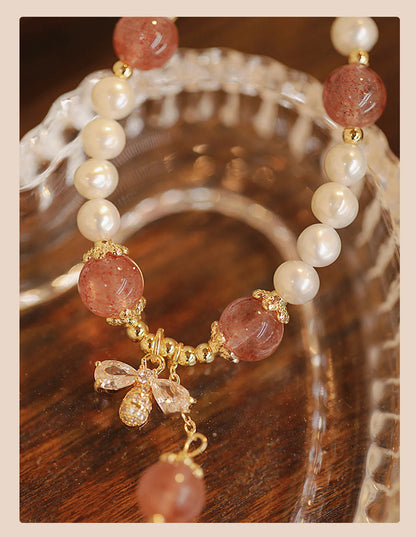 Women's strawberry quartz crystal bracelet with a decorative bow charm on a wrist.
