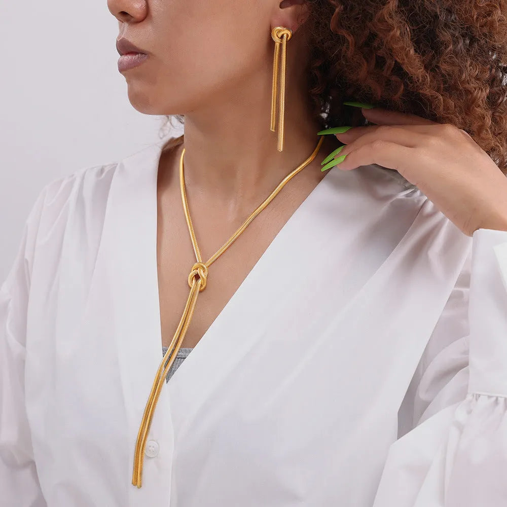 Gold electroplated titanium steel necklace with snake chain and knotted tassel pendant, shown with matching earrings.