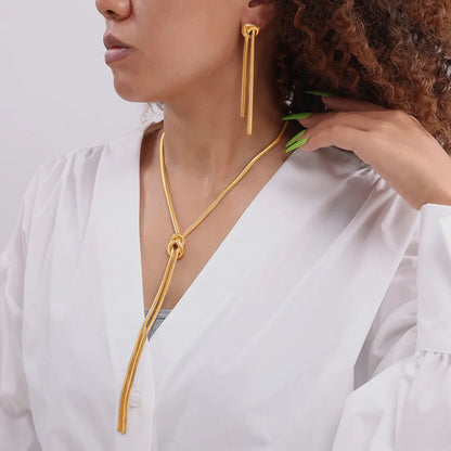 Gold electroplated titanium steel necklace with snake chain and knotted tassel pendant, shown with matching earrings.