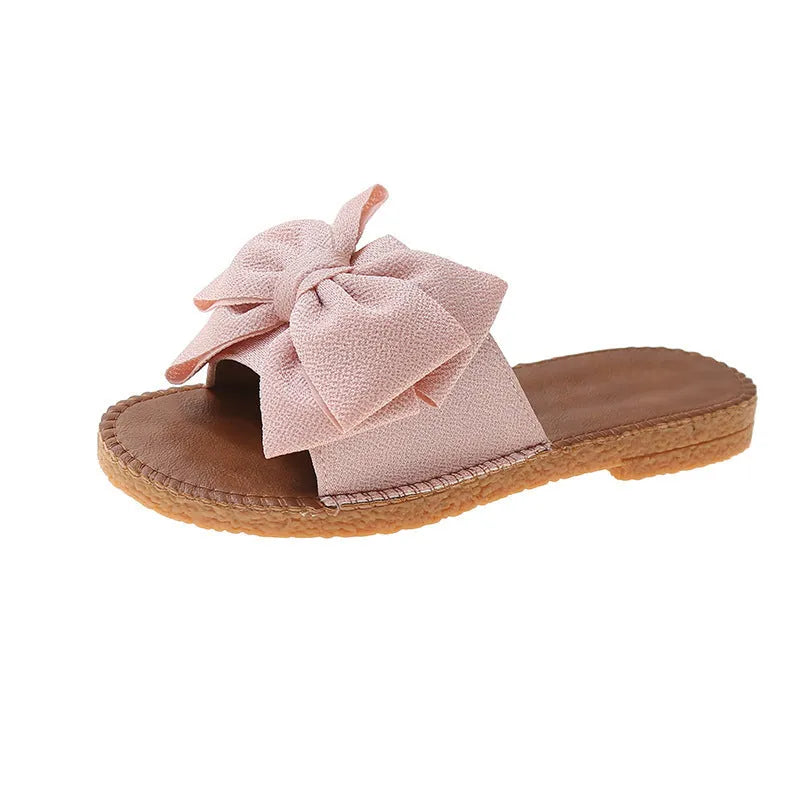 Women's beige suede slip-on sandals with a bow detail and soft rubber flat sole.