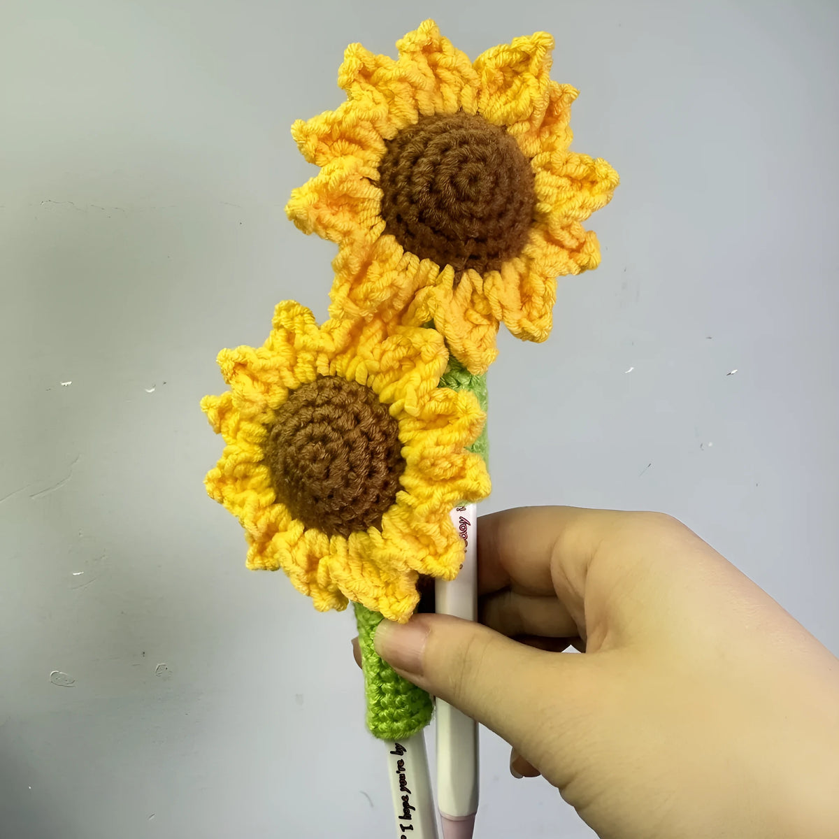 Hand-woven yellow and brown sunflower pen cover holding a pen.
