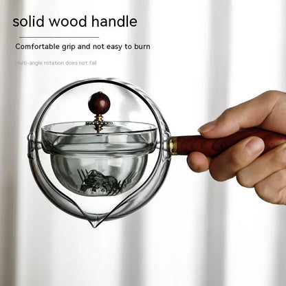 Transparent borosilicate glass rotary teapot with wooden handle and built-in infuser on a wooden surface