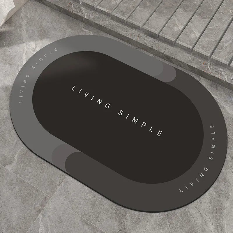 Oval grey bath mat with non-slip rubber bottom on a tiled floor, showing absorbent fabric surface