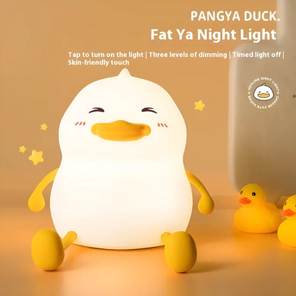 Chubby Night Light, a soft-grey silicone phone holder on top of a white plastic base, glowing with a warm light on a wooden desk.