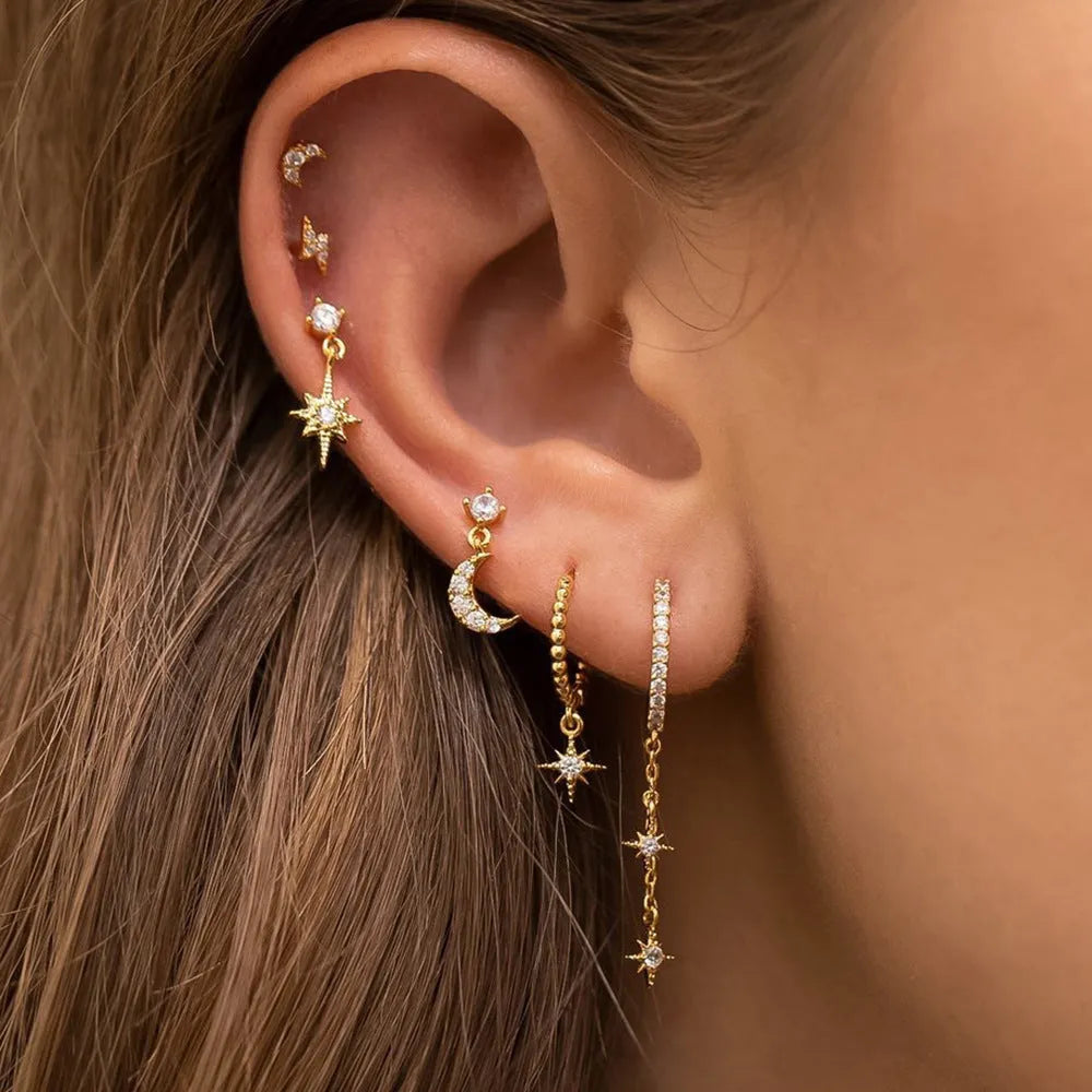 Set of six gold-coloured XINGX chain tassel stud earrings with zircon details on a flat surface.