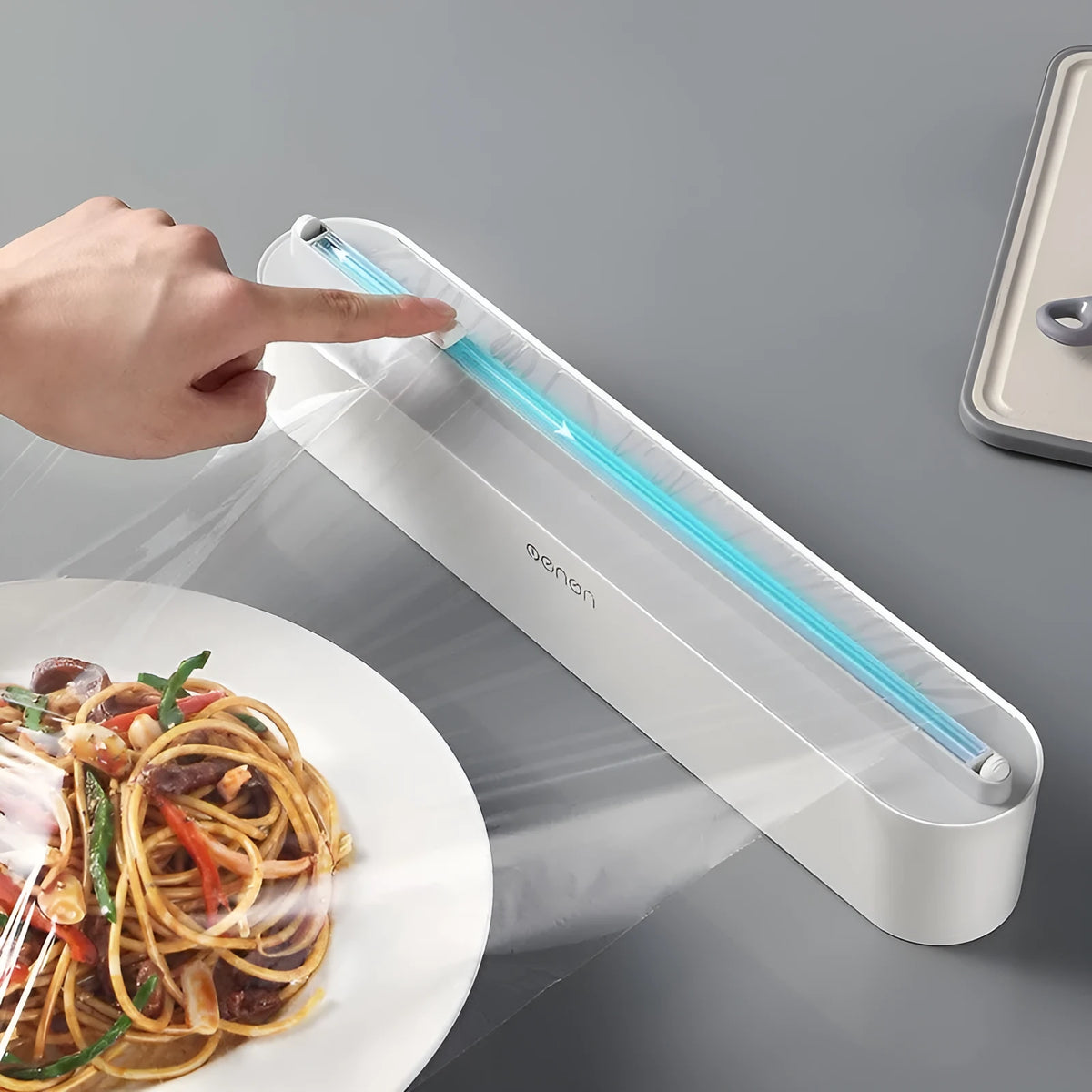 Black plastic cling film cutter and dispenser unit mounted on a refrigerator door.