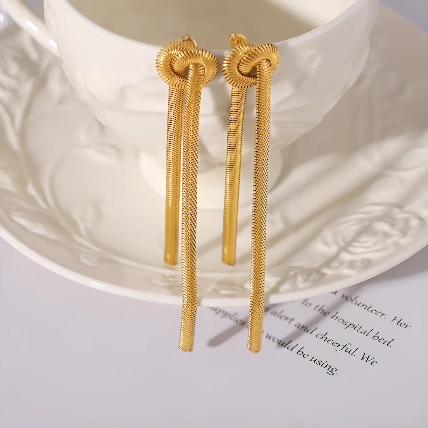 Gold electroplated titanium steel necklace with snake chain and knotted tassel pendant, shown with matching earrings.