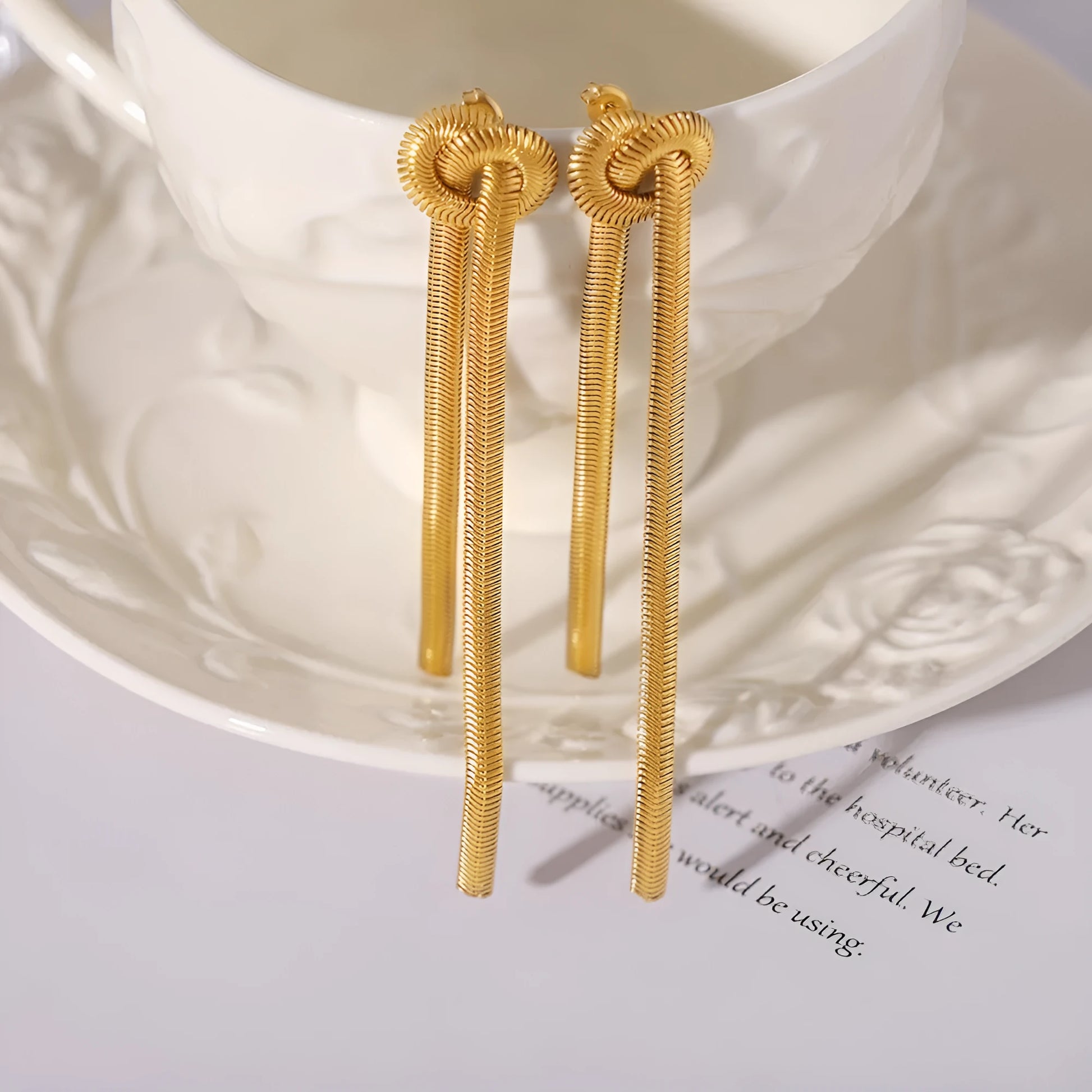 Gold electroplated titanium steel necklace with snake chain and knotted tassel pendant, shown with matching earrings.