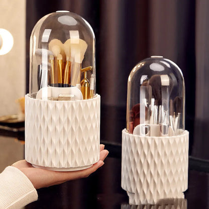 White rotating acrylic makeup brush holder with transparent dustproof lid on a desktop.