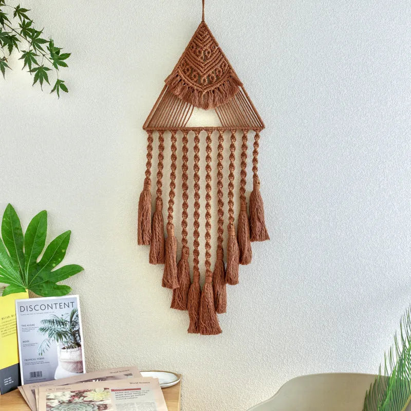 Large white handwoven triangle dream catcher pendant with wooden beads and a long tassel hanging on a wall.