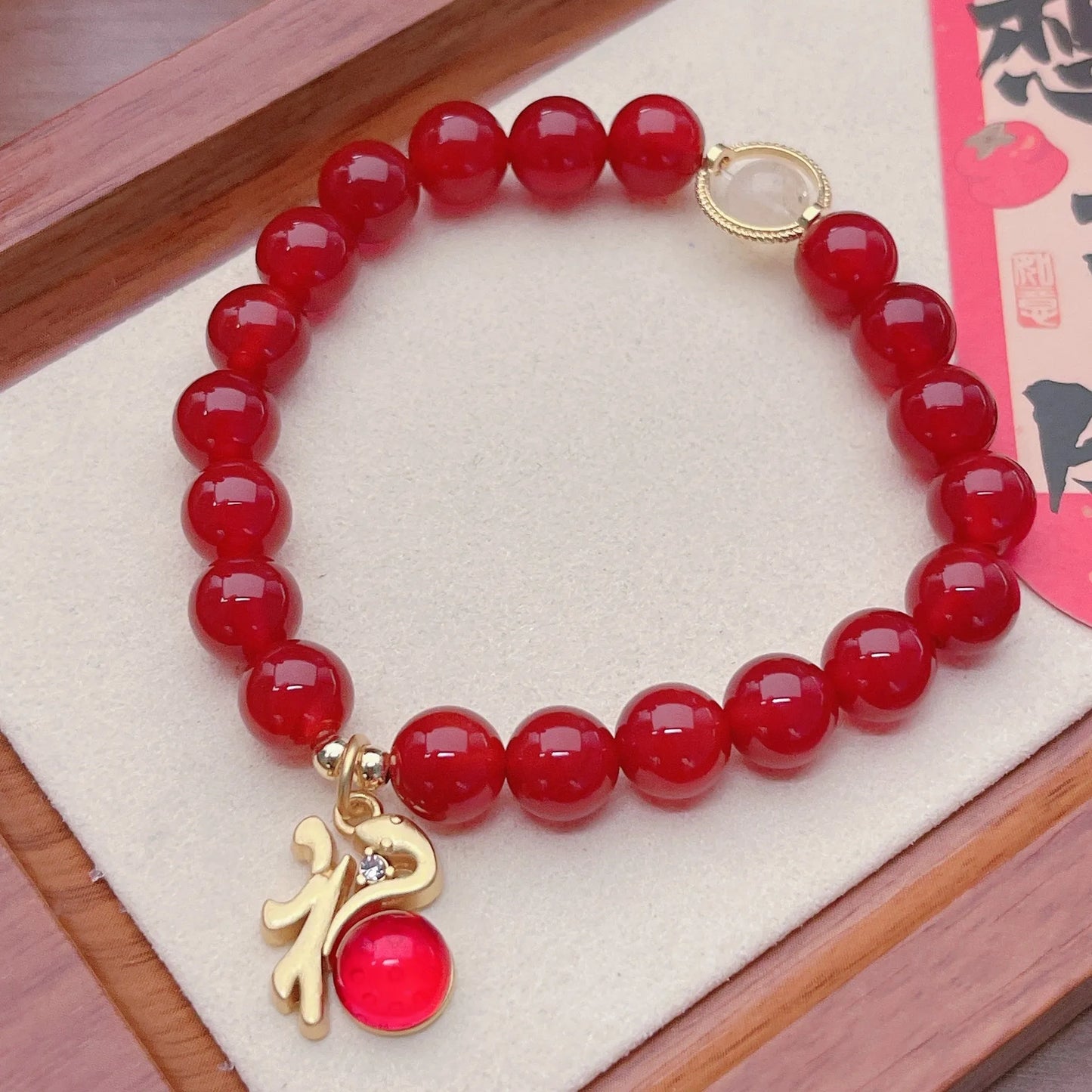 Close-up of a red agate bracelet with a dragon charm and Lucky Bag symbol on a wrist.