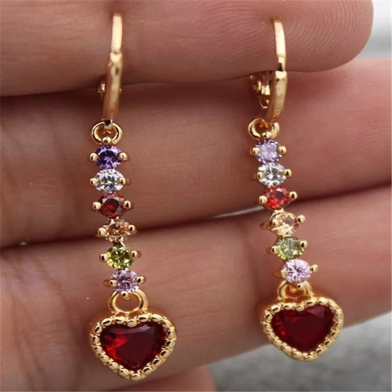 A pair of small gold-coloured heart-shaped alloy earrings on a plain background.