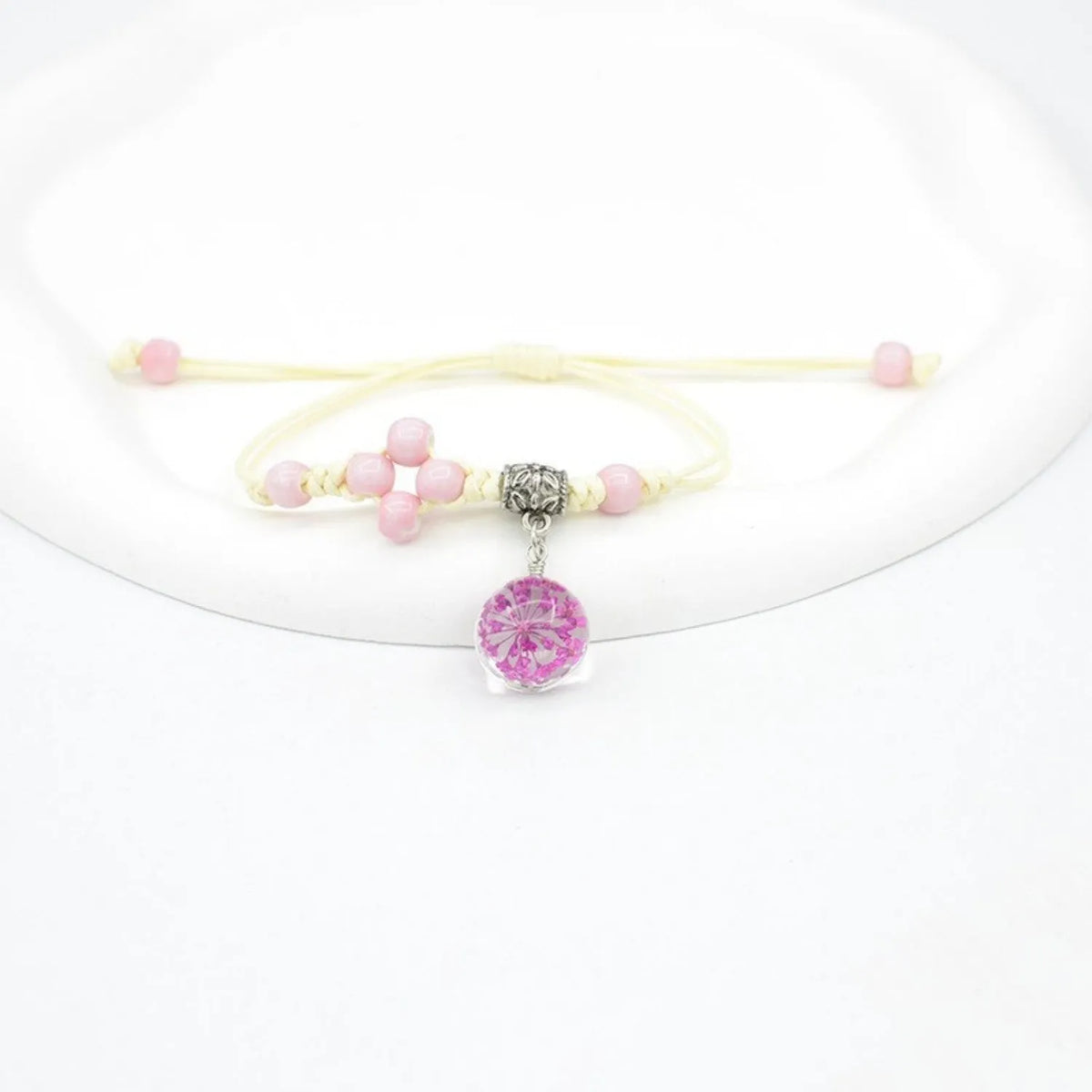 Close-up of a hand-woven bracelet with a large 1.4cm glass bead containing colourful dried flowers.