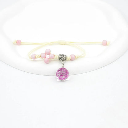 Close-up of a hand-woven bracelet with a large 1.4cm glass bead containing colourful dried flowers.