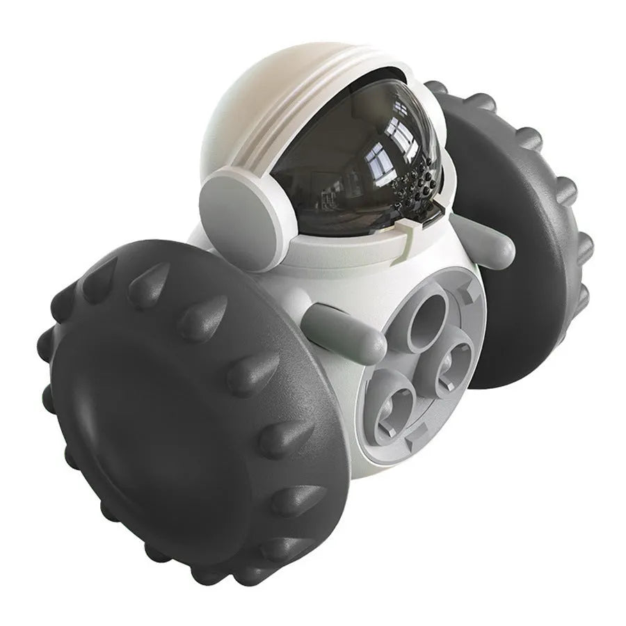 A black, robot-shaped treat dispenser toy for dogs and cats on a wooden floor, showing its size and rolling design.