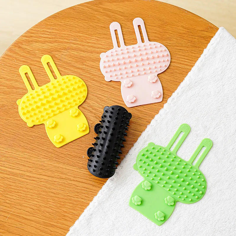 Silicone cat grooming comb with adjustable strap mounted on a table leg, shown in green.