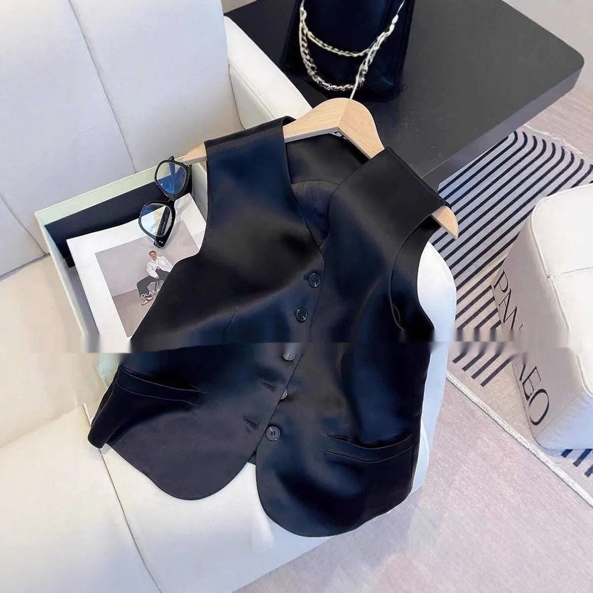 Black satin sleeveless vest on a hanger, showing loose fit and splicing detail.