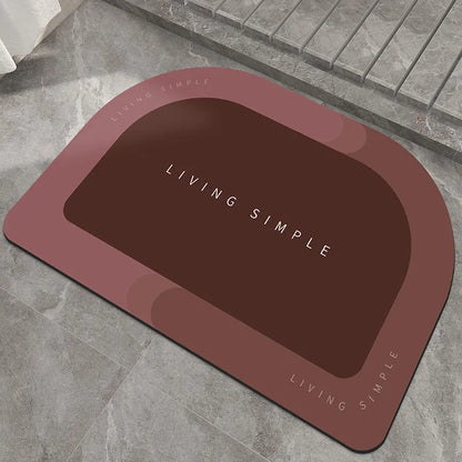 Oval grey bath mat with non-slip rubber bottom on a tiled floor, showing absorbent fabric surface