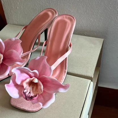Pink women's sandals with a satin upper, artificial white Phalaenopsis flower, square toe, and a mid-height heel.