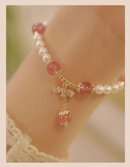Women's strawberry quartz crystal bracelet with a decorative bow charm on a wrist.
