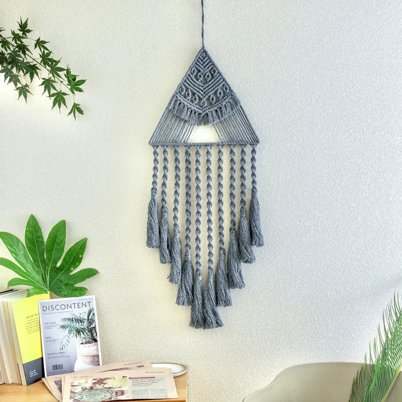 Large white handwoven triangle dream catcher pendant with wooden beads and a long tassel hanging on a wall.