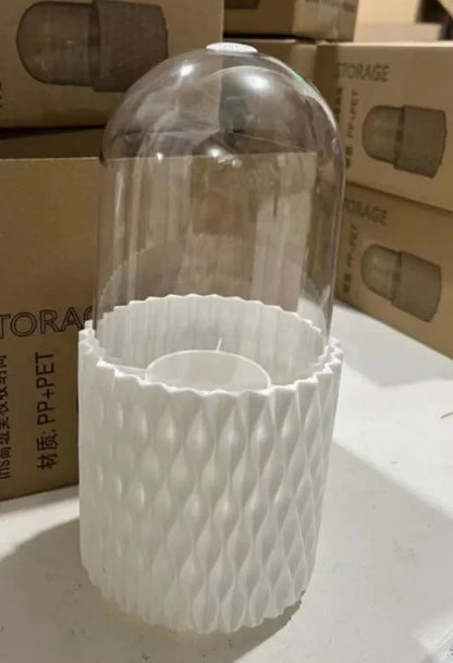 White rotating acrylic makeup brush holder with transparent dustproof lid on a desktop.